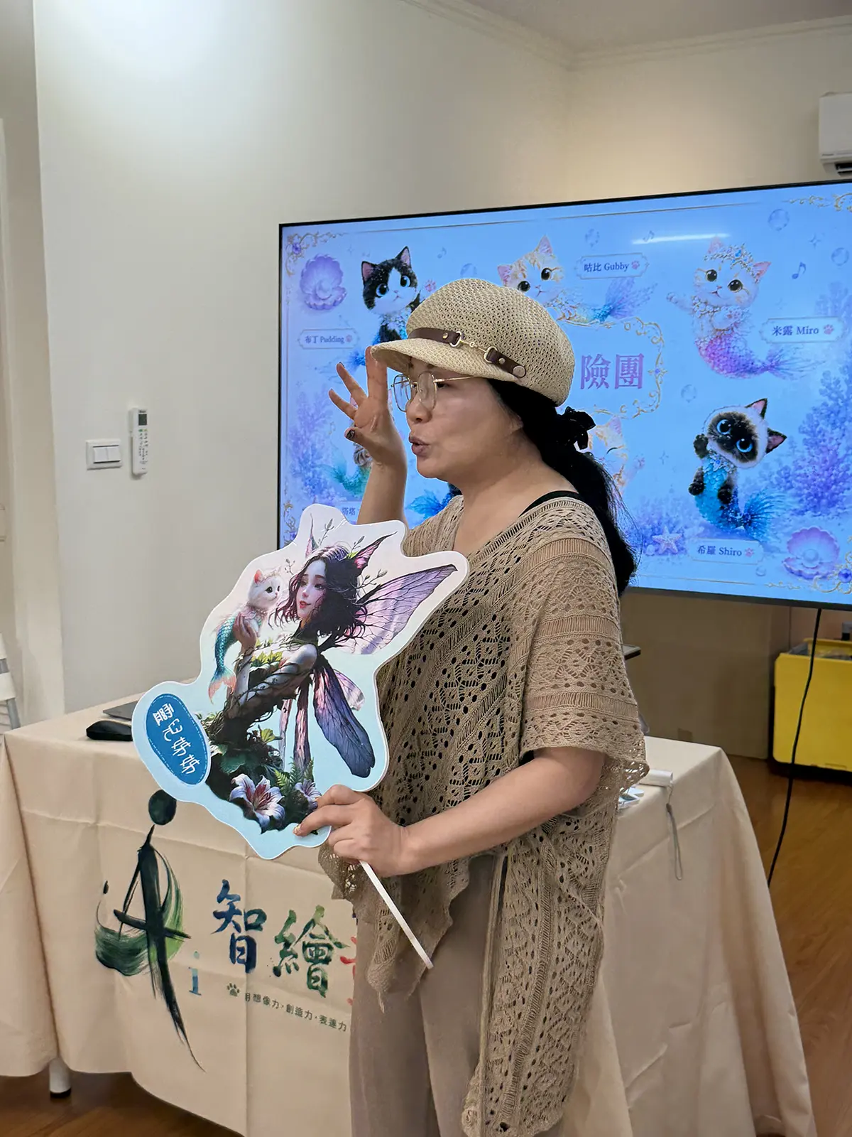 老師拿著喵精靈角色立牌，在投影喵精靈冒險團的螢幕前帶孩子進入故事